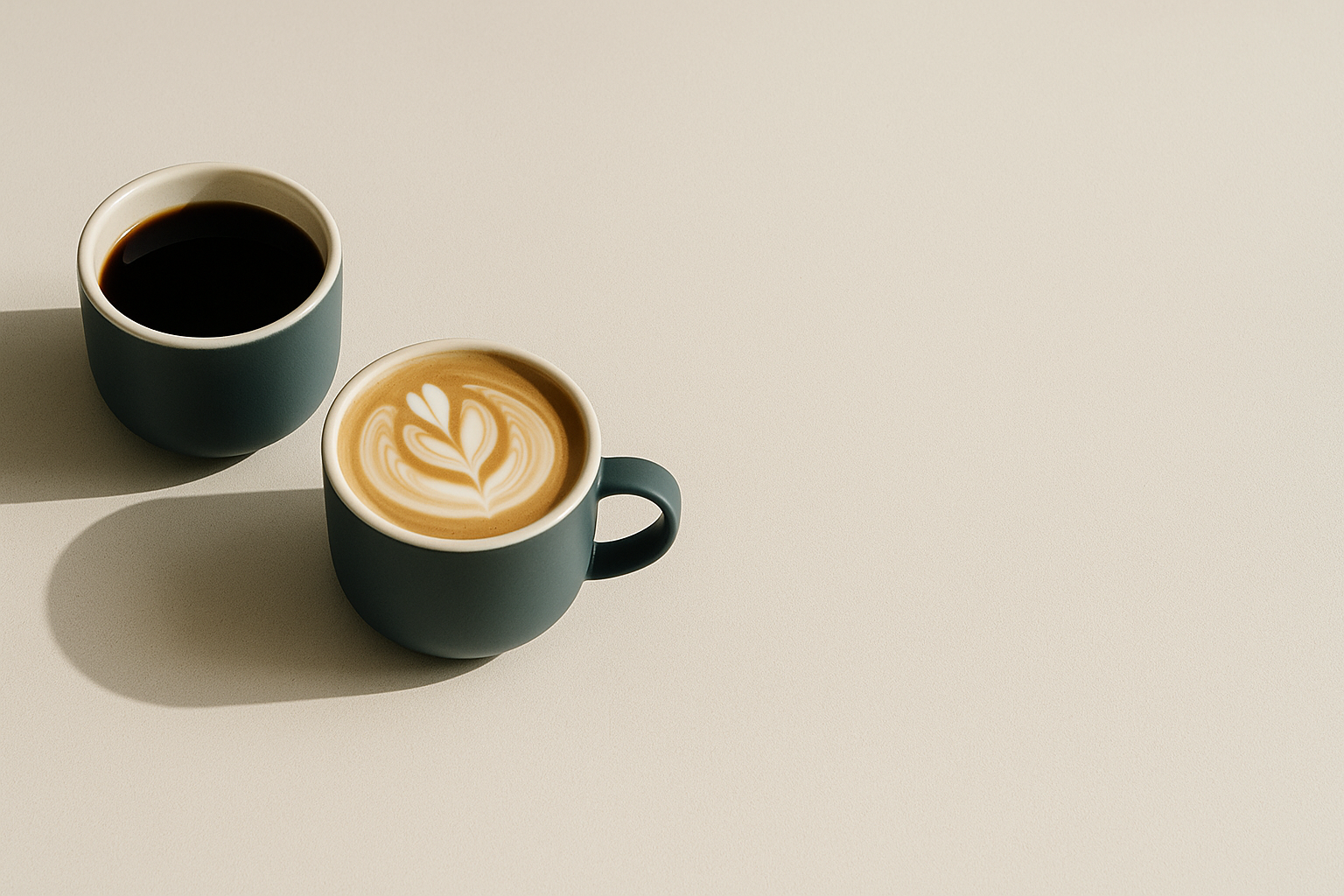 Two coffee cups on a beige background, one with a leaf design in the foam.