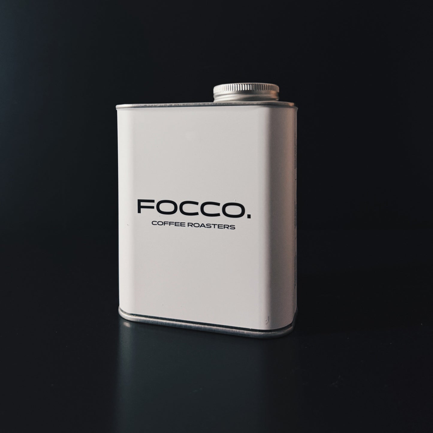A white rectangular metal canister with a silver screw cap, featuring the black text 'FOCCO. COFFEE ROASTERS' on the front, set against a dark black background.