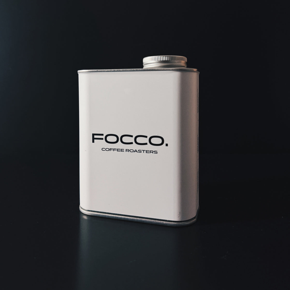 A white rectangular metal canister with a silver screw cap, featuring the black text 'FOCCO. COFFEE ROASTERS' on the front, set against a dark black background.