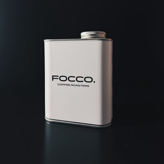 A white rectangular metal canister with a silver screw cap, featuring the black text 'FOCCO. COFFEE ROASTERS' on the front, set against a dark black background.