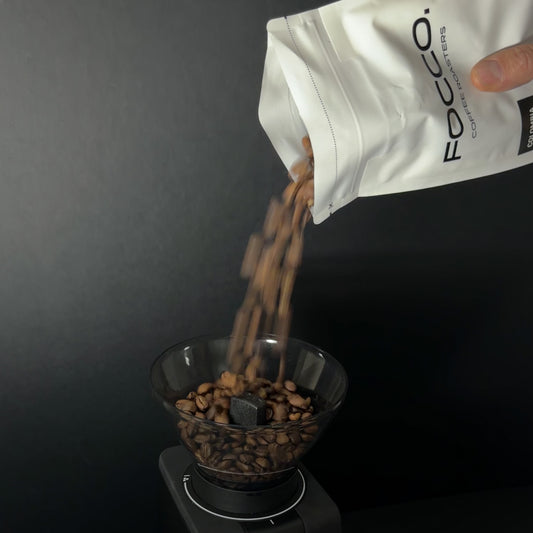 Coffee beans being poured from a bag labeled 'FOCO' into a grinder.