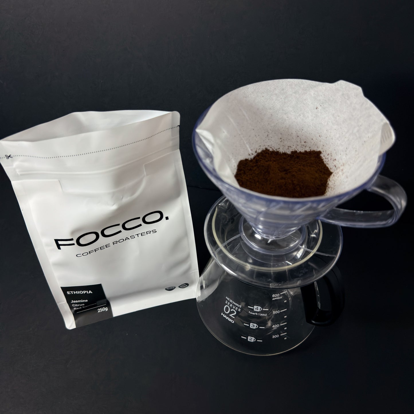 FOCCO coffee bag and a glass coffee filter with ground coffee on a black background
