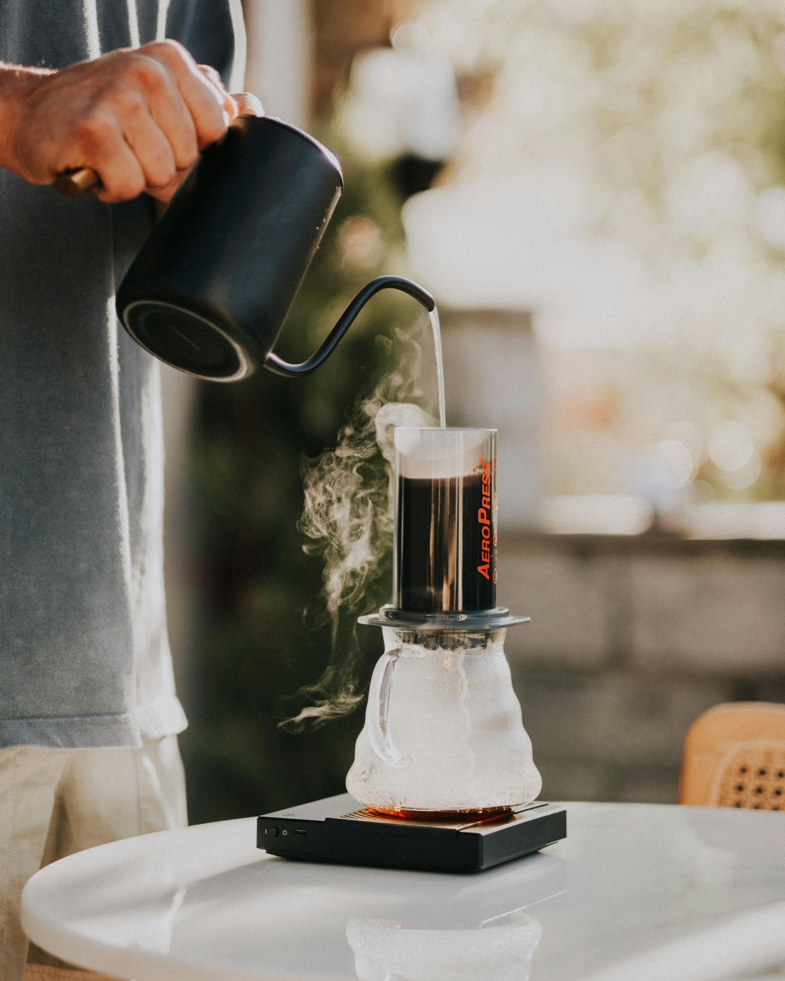 Person pouring coffee into an Aeropress on a table outdoors.